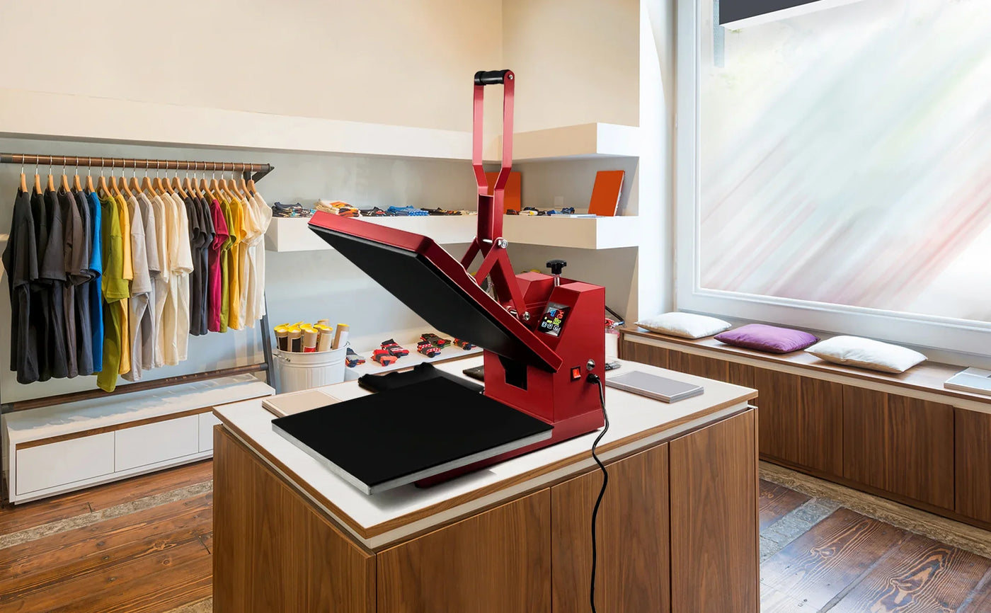 Red heat press machine on a wooden table in a bright shop, with colorful t-shirts hanging on the wall and a cozy seating area nearby
