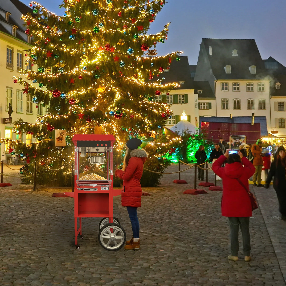 Bright red KuKoo popcorn machine cart with glass display, set against a festive Christmas tree in a bustling market square