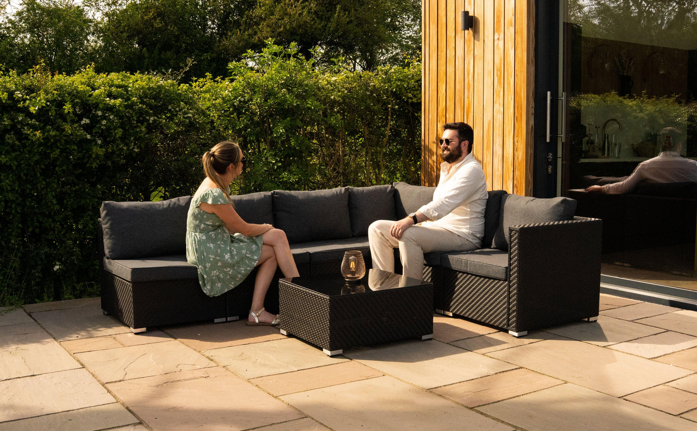 Stylish outdoor seating set featuring a dark wicker sectional sofa with gray cushions, complemented by a glass-top coffee table