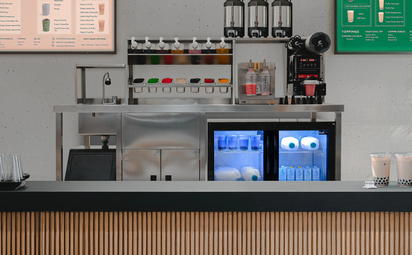 Modern beverage counter featuring a sleek stainless steel design, colorful syrup dispensers, and a glass-front refrigerator showcasing drinks