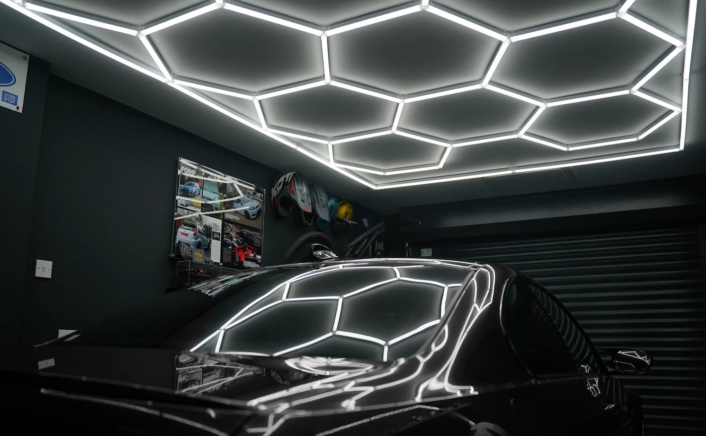 Sleek black car parked under a modern hexagonal LED ceiling, reflecting light patterns on its polished surface in a stylish garage