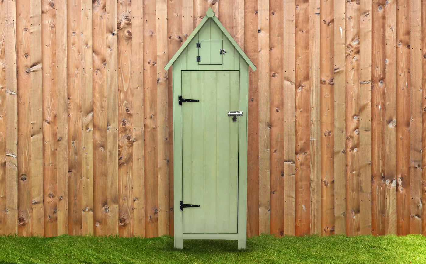 Charming green wooden shed with a house-shaped roof, black metal hinges, and a rustic wooden backdrop on grassy ground