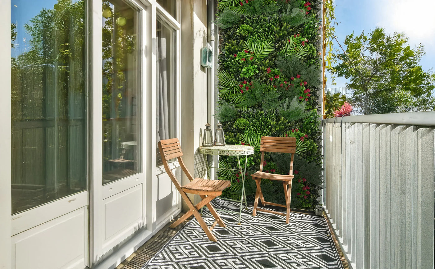 Cozy balcony with two wooden chairs, a round table, and a lush green wall of plants, featuring a geometric black and white rug