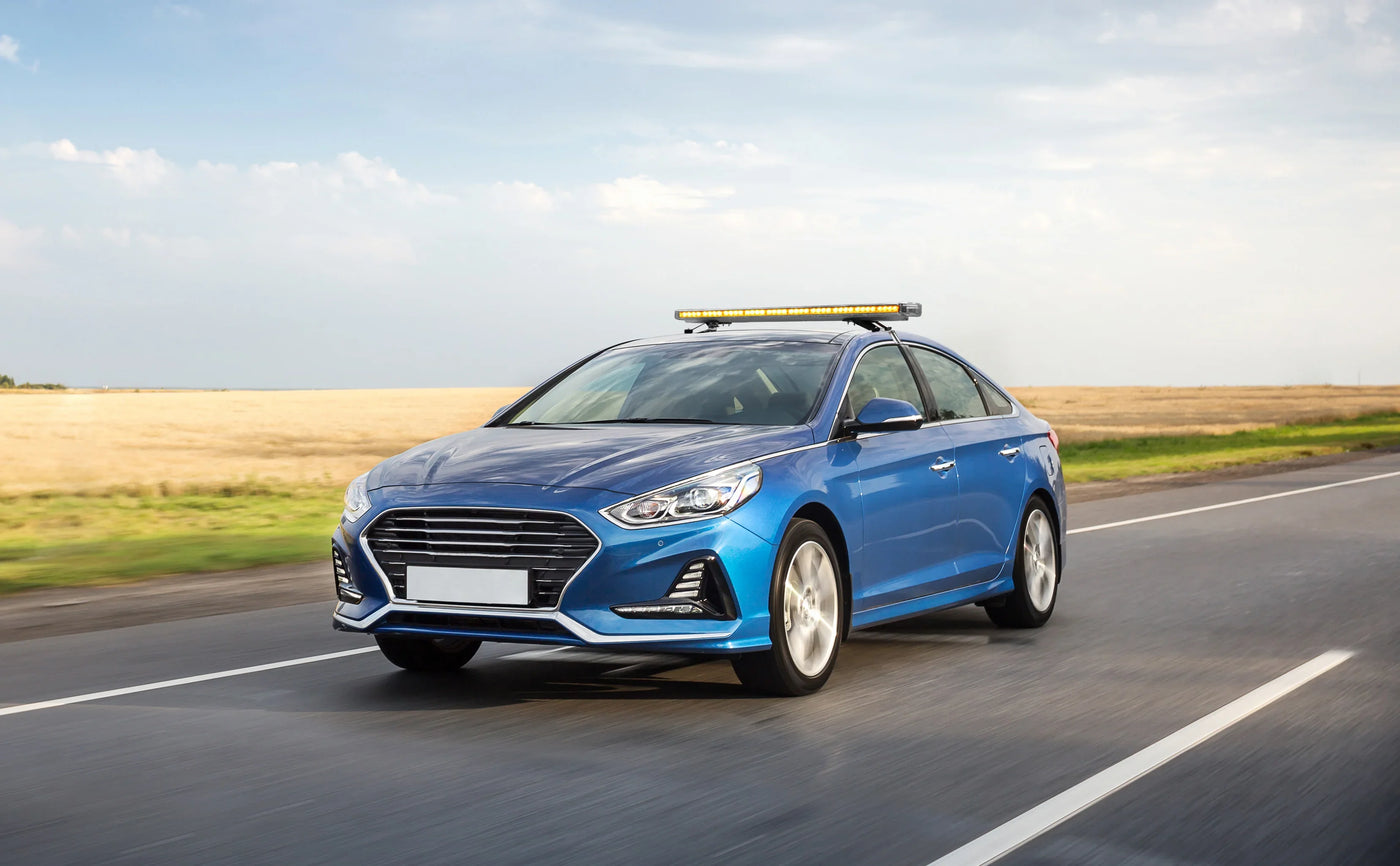 Blue sedan with a sleek design and a light bar on top, driving on a highway with a vast field in the background