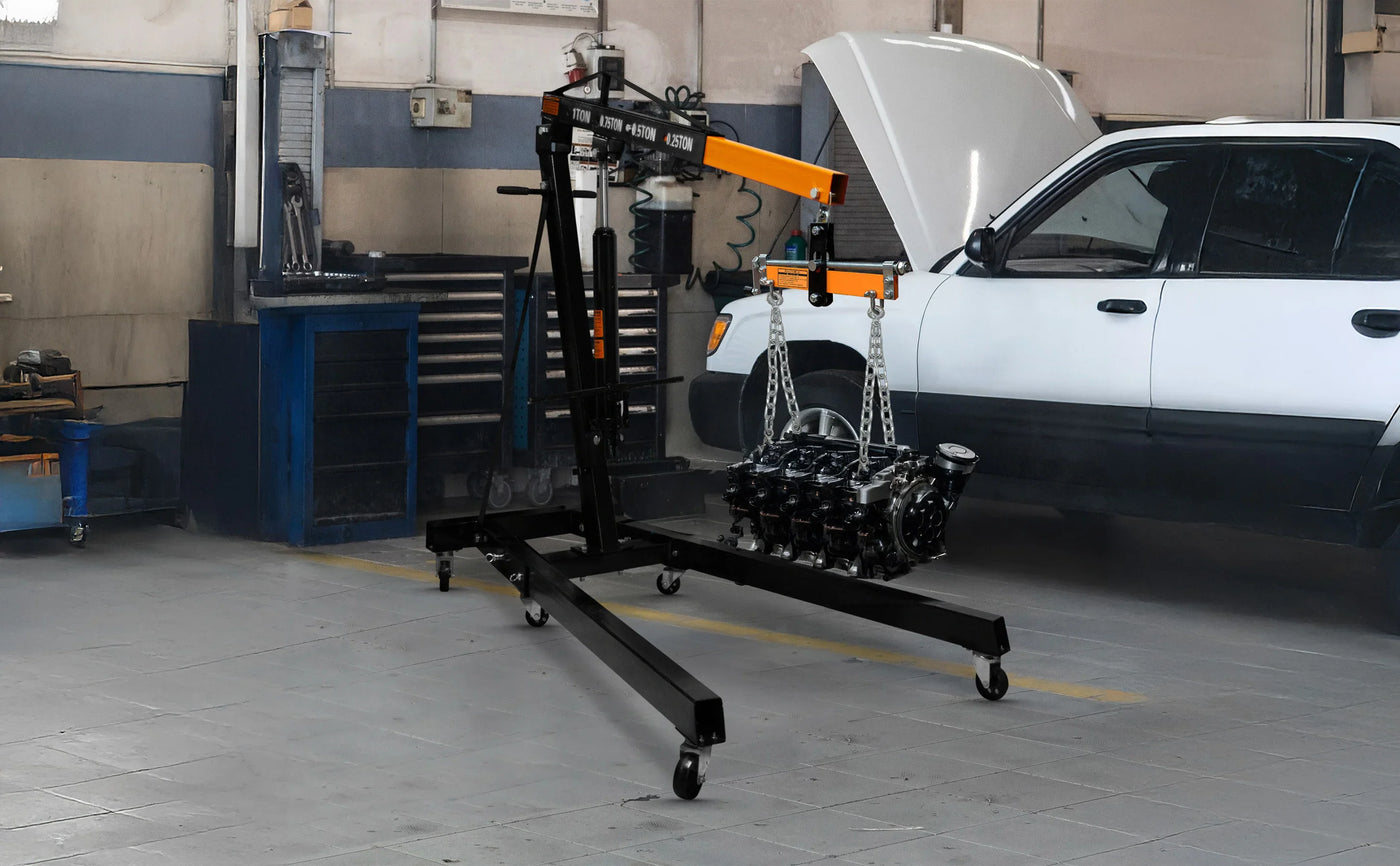 Heavy-duty engine hoist in a garage, featuring a sturdy black frame, orange arm, and an engine suspended by chains for easy lifting