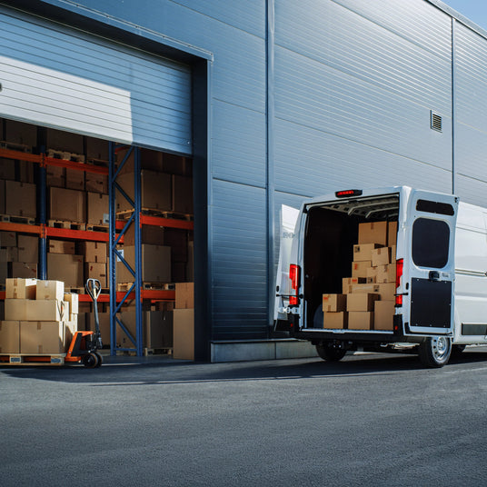 Delivery van parked beside a warehouse, filled with stacked cardboard boxes, showcasing a busy logistics environment