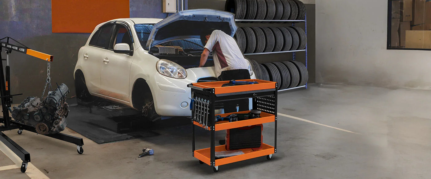Mechanic working on a white car in a garage with tool cart and tire rack.
