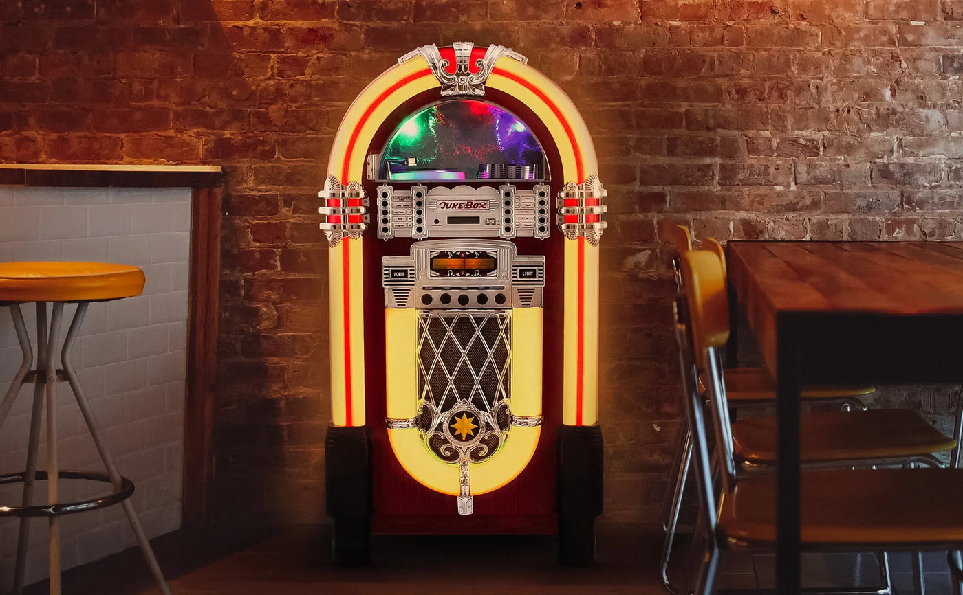 Vintage jukebox with a glossy red and yellow exterior, chrome accents, and illuminated edges, set against a rustic brick wall