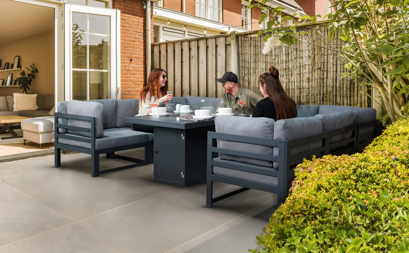 Cozy outdoor seating area with gray cushioned sofas, a black table, and friends enjoying tea in a sunny garden setting