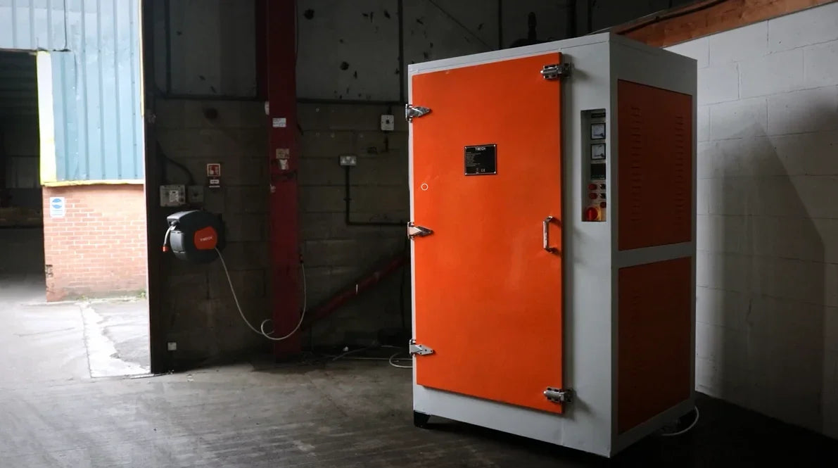 Industrial orange and white drying cabinet with metal handles, located in a warehouse setting with exposed concrete walls and red beams