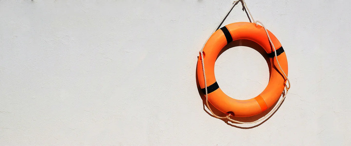 Bright orange life ring with black stripes, hanging on a white wall, showcasing a smooth, glossy texture and sturdy rope