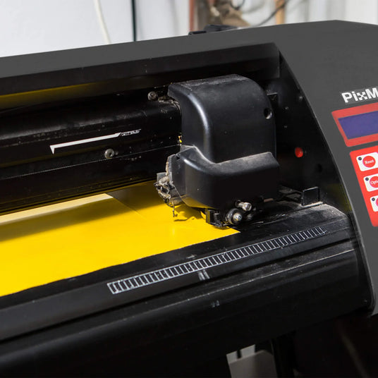 Black cutting machine with a sleek design, featuring a yellow cutting mat and precise blade for crafting and design projects