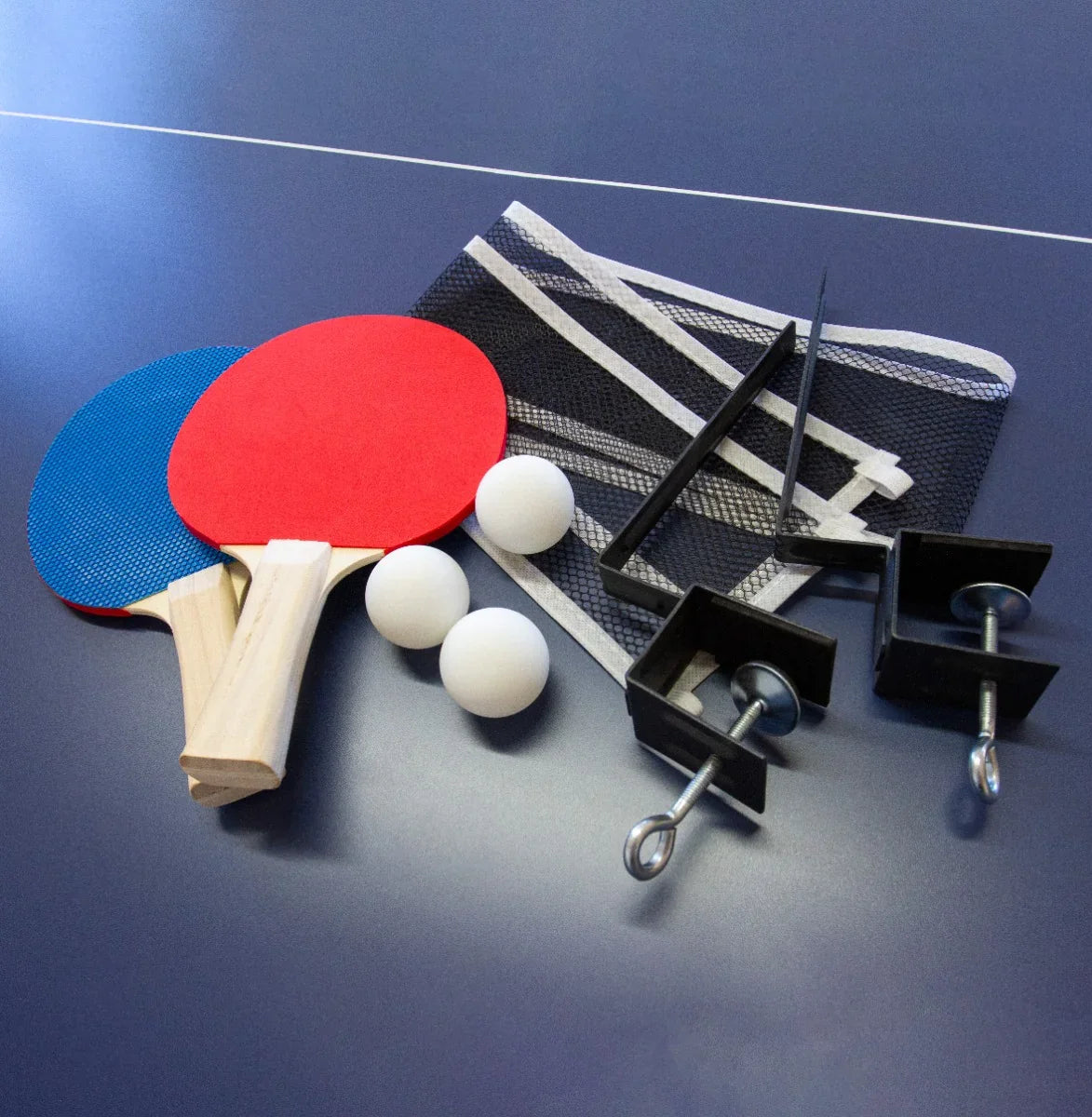 Red and blue table tennis paddles, three white balls, a black net, and clamps arranged on a blue table surface