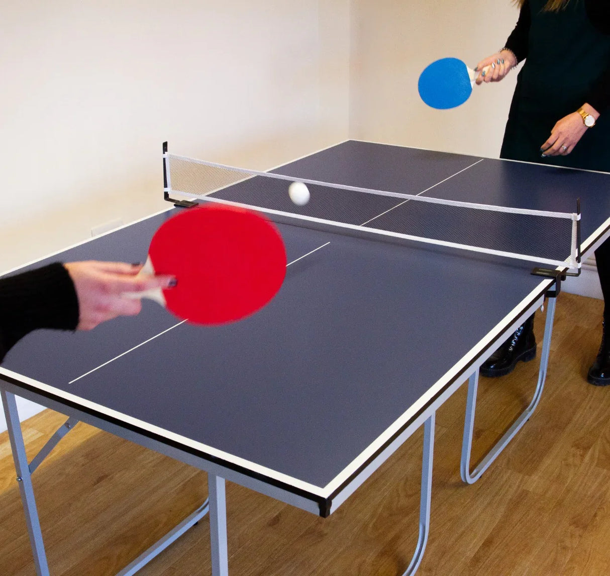 Folding table tennis table with a blue and red paddle in action, featuring a sleek dark surface and sturdy folding legs