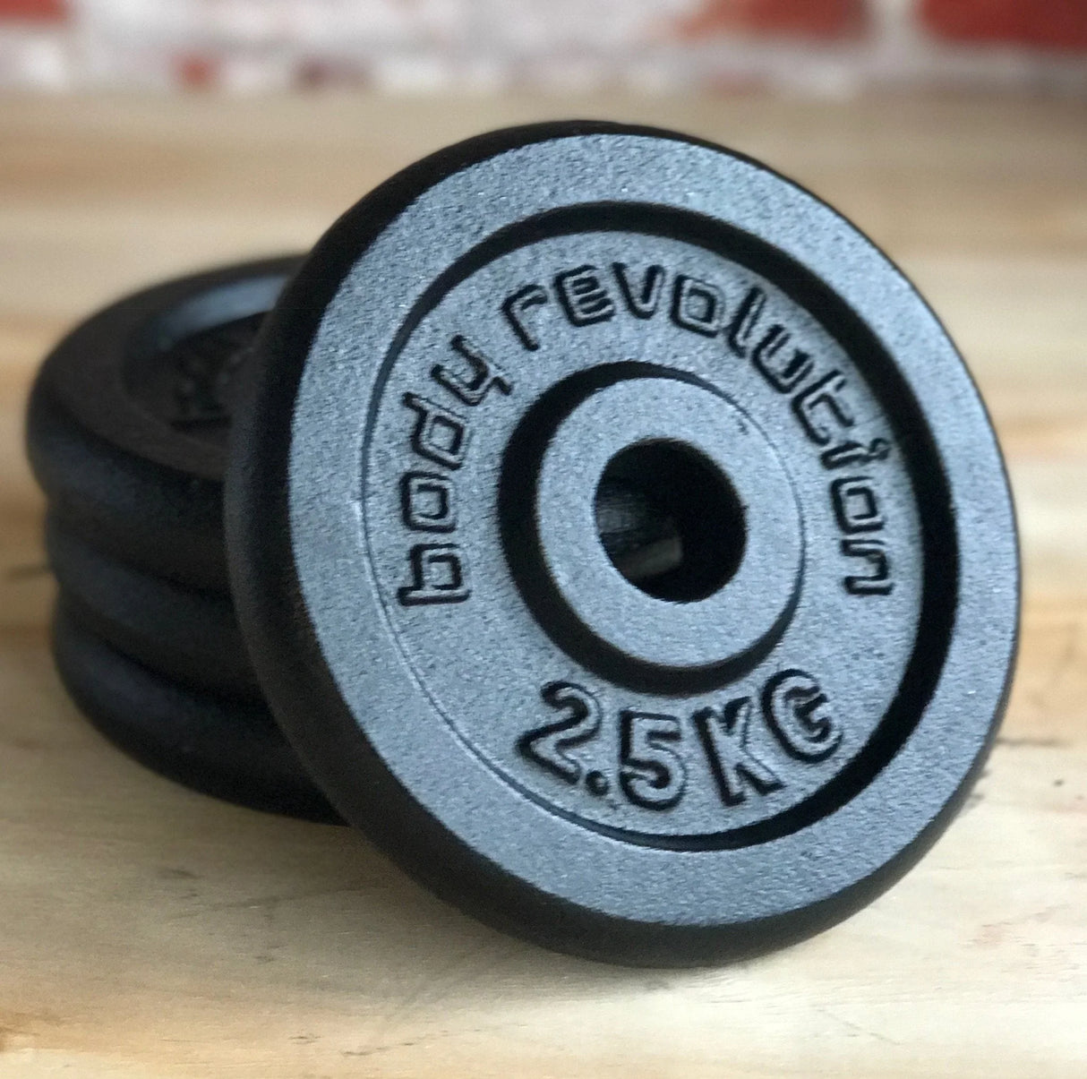 Black cast iron weight plates with raised lettering, featuring a 2.5 kg weight and a smooth, durable finish, stacked on a wooden surface