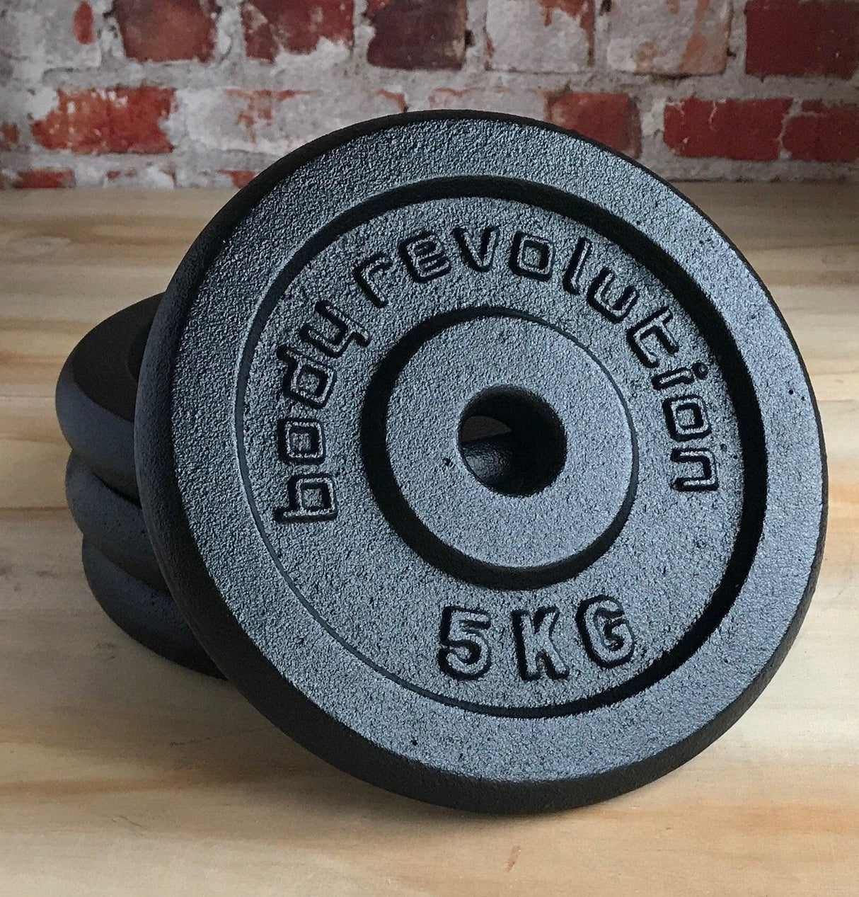 5kg cast iron weight plates with a textured surface and bold lettering, stacked against a rustic brick background