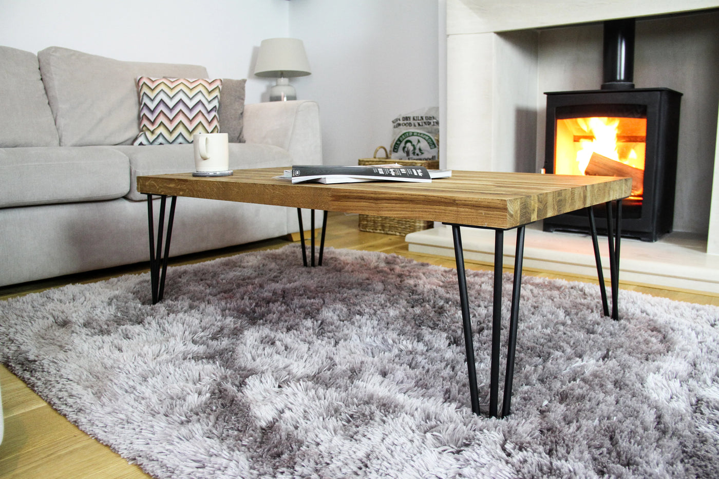 Rustic wooden coffee table with black metal legs, placed on a soft, fluffy gray rug in a cozy living room with a fireplace