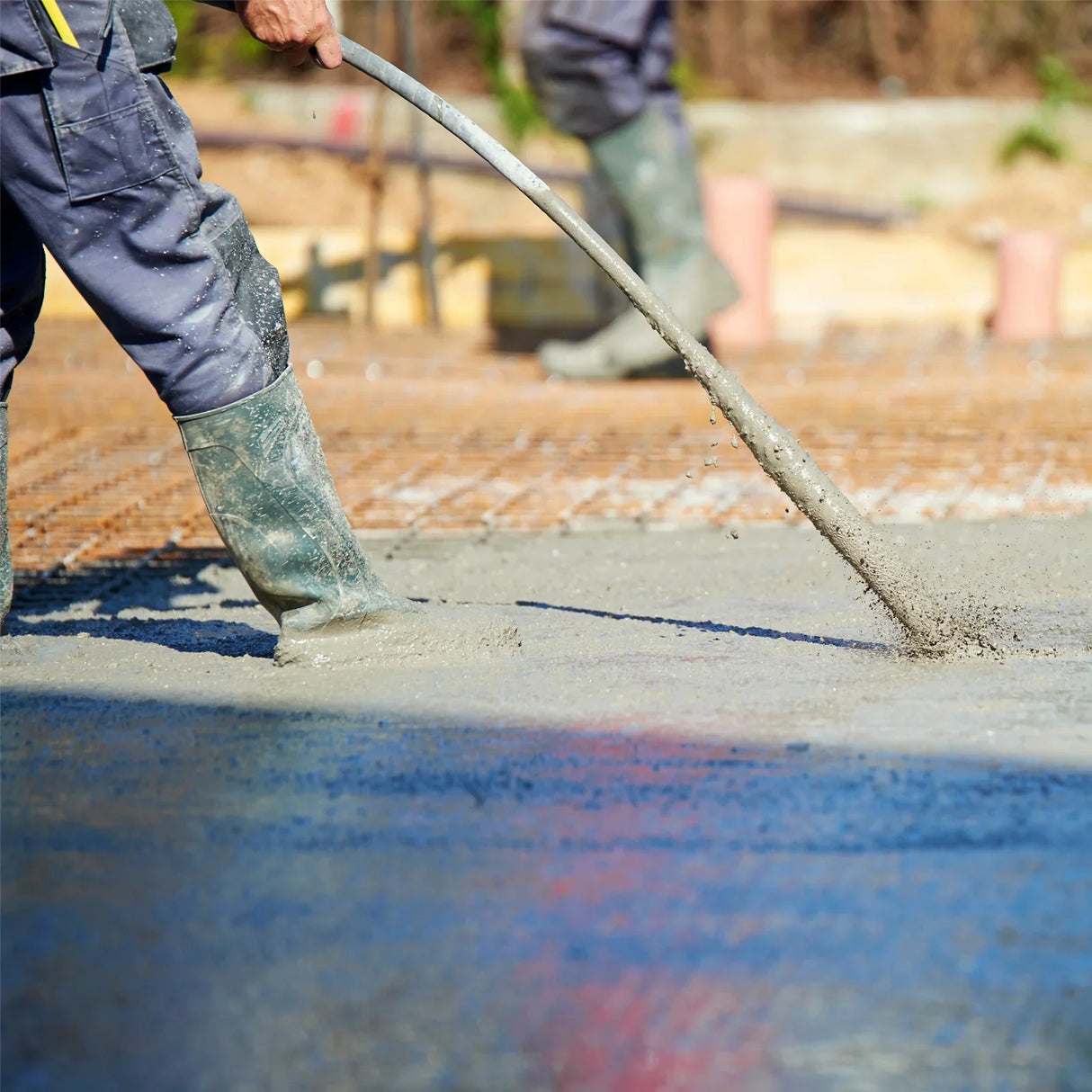 T-Mech Concrete Vibrator in use, smoothing wet concrete surface with a flexible shaft, worker in waterproof boots on site