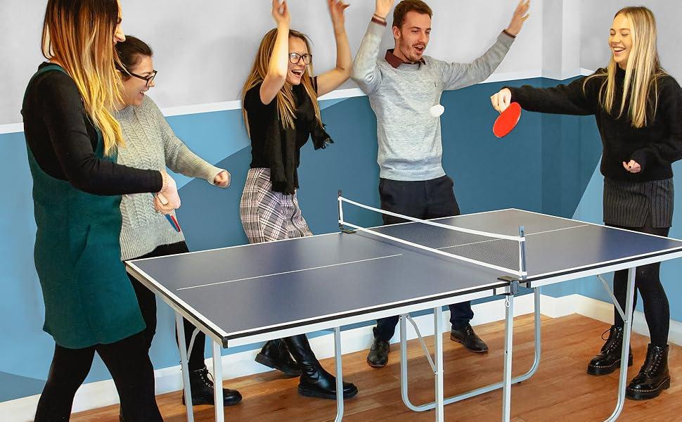 Group of five young adults enjoying a lively game of table tennis, with smiles, laughter, and colorful paddles in a bright room
