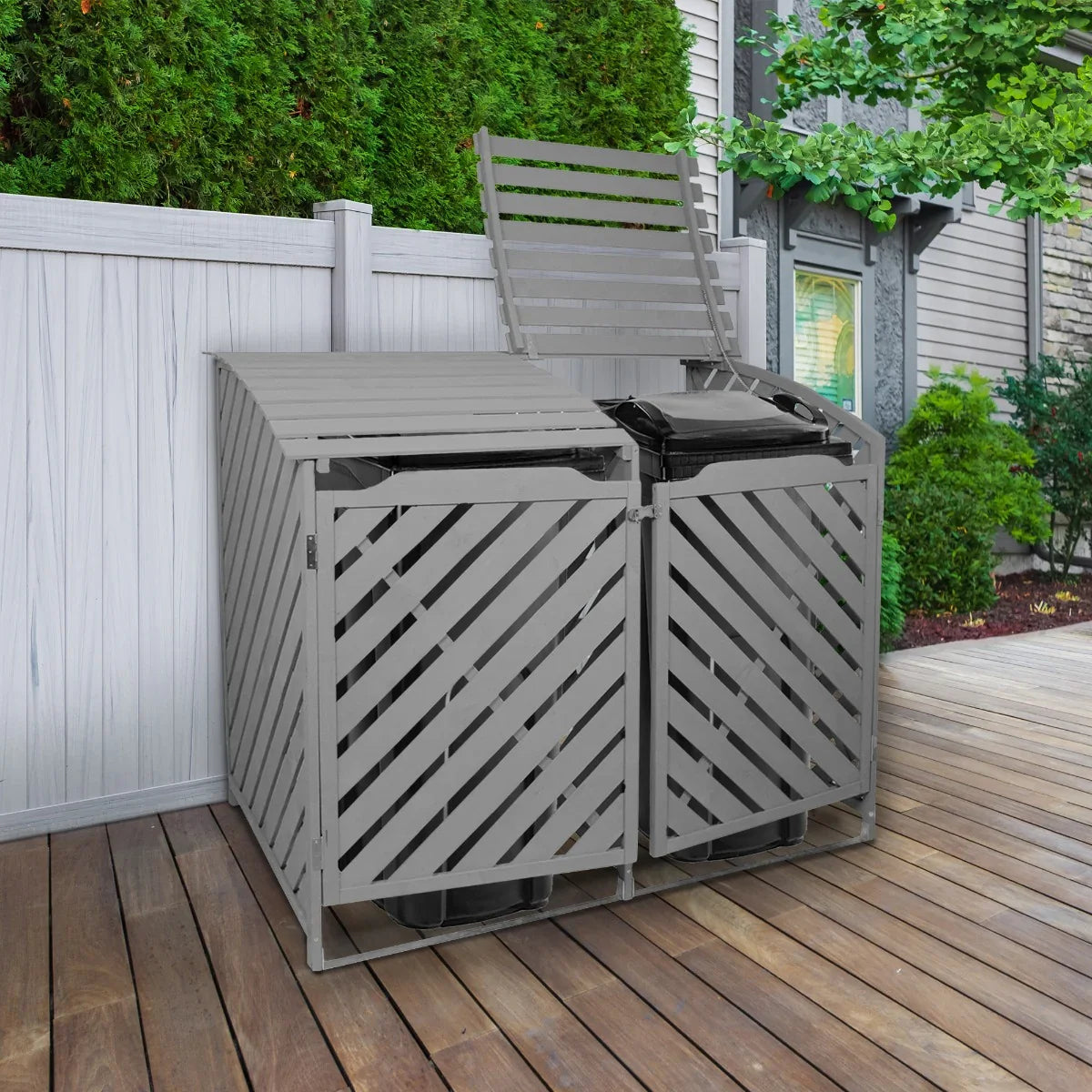 Grey wash double wheelie bin storage with slatted design, featuring two compartments for bins, set on a wooden deck with greenery in the background
