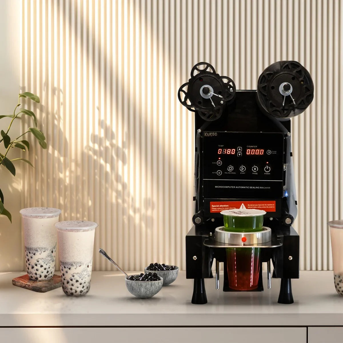 Automatic cup sealing machine in sleek black with digital display, sealing cups of bubble tea and toppings on a modern countertop