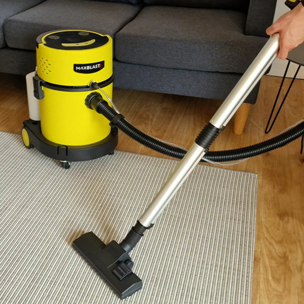 MAXBLAST 20L wet and dry vacuum cleaner in bright yellow with a stainless steel handle, being used on a textured rug in a modern living room