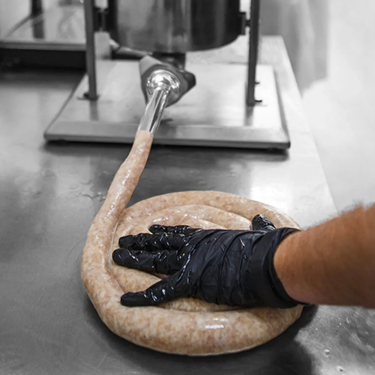 Kukoo 7 Litre Sausage Stuffer in use, with a hand pressing freshly made sausage in a smooth, coiled shape on a stainless steel surface
