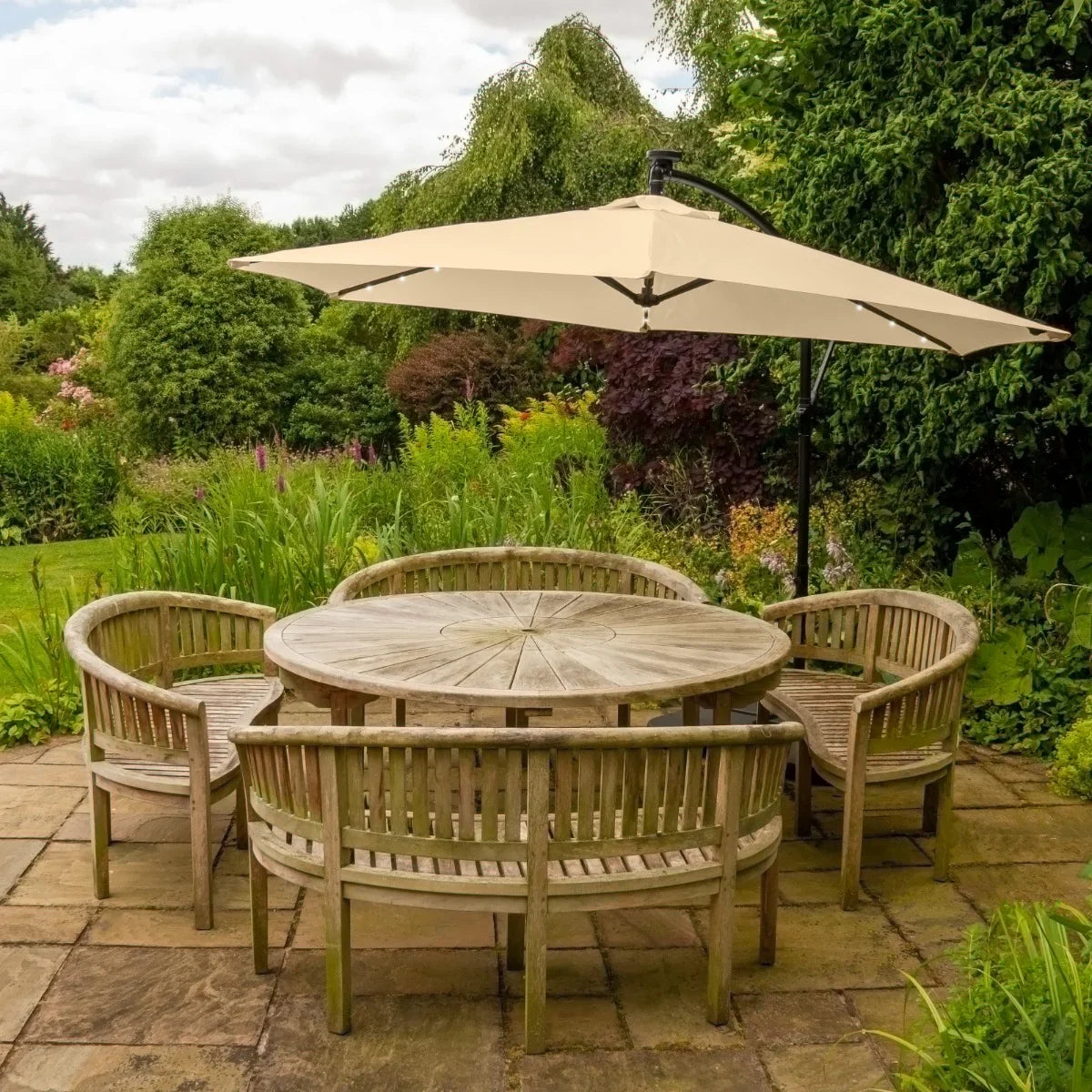Beige 3m LED cantilever parasol with plain base, providing shade over a round wooden table and curved benches in a lush garden setting