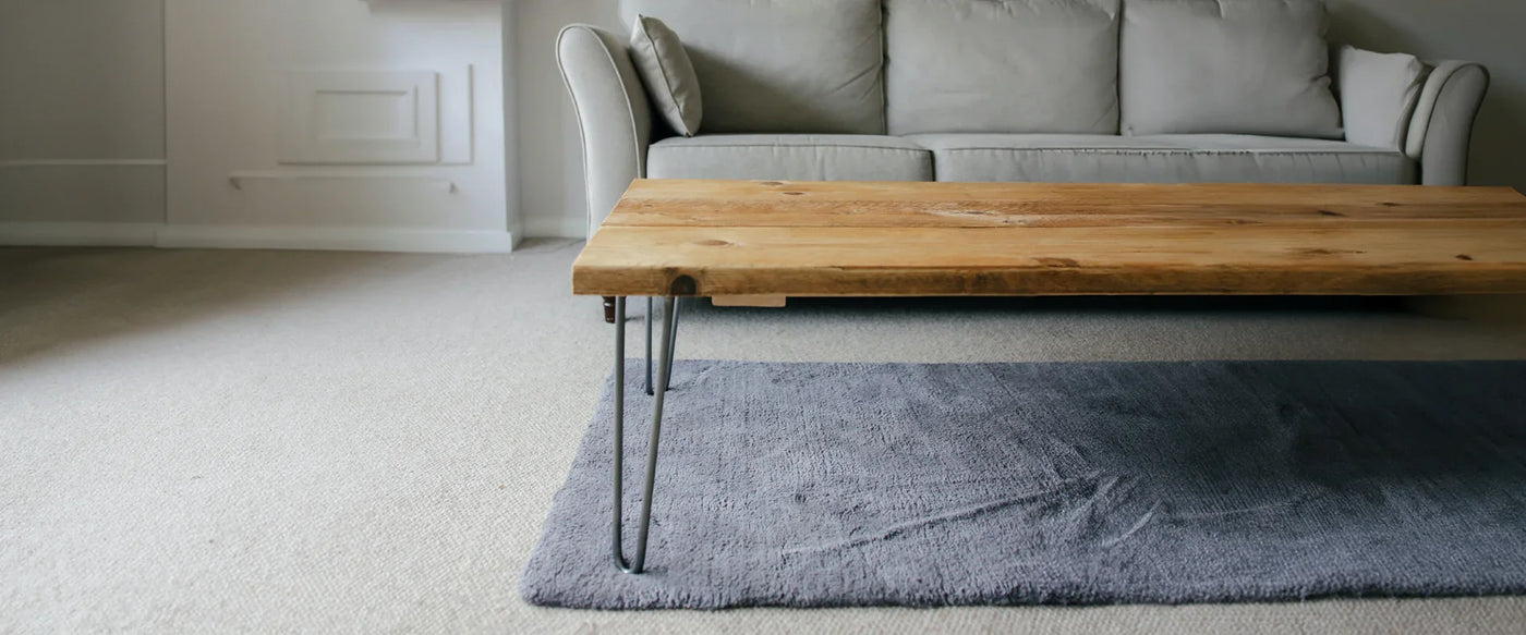 Rustic wooden coffee table with metal legs on a soft gray rug, set in a cozy living room with a light gray sofa in the background