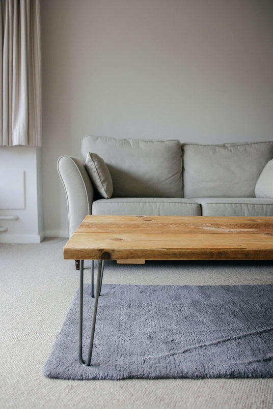 Rustic wooden coffee table with metal legs, placed on a soft gray rug, beside a light gray sofa in a cozy living room setting