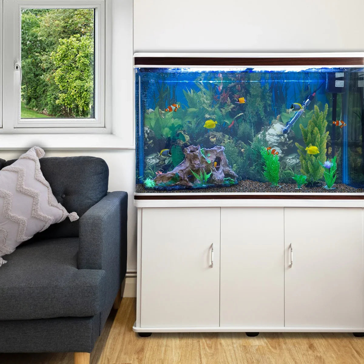 White aquarium fish tank with natural gravel, vibrant plants, and colorful fish, displayed on a sleek cabinet beside a cozy couch