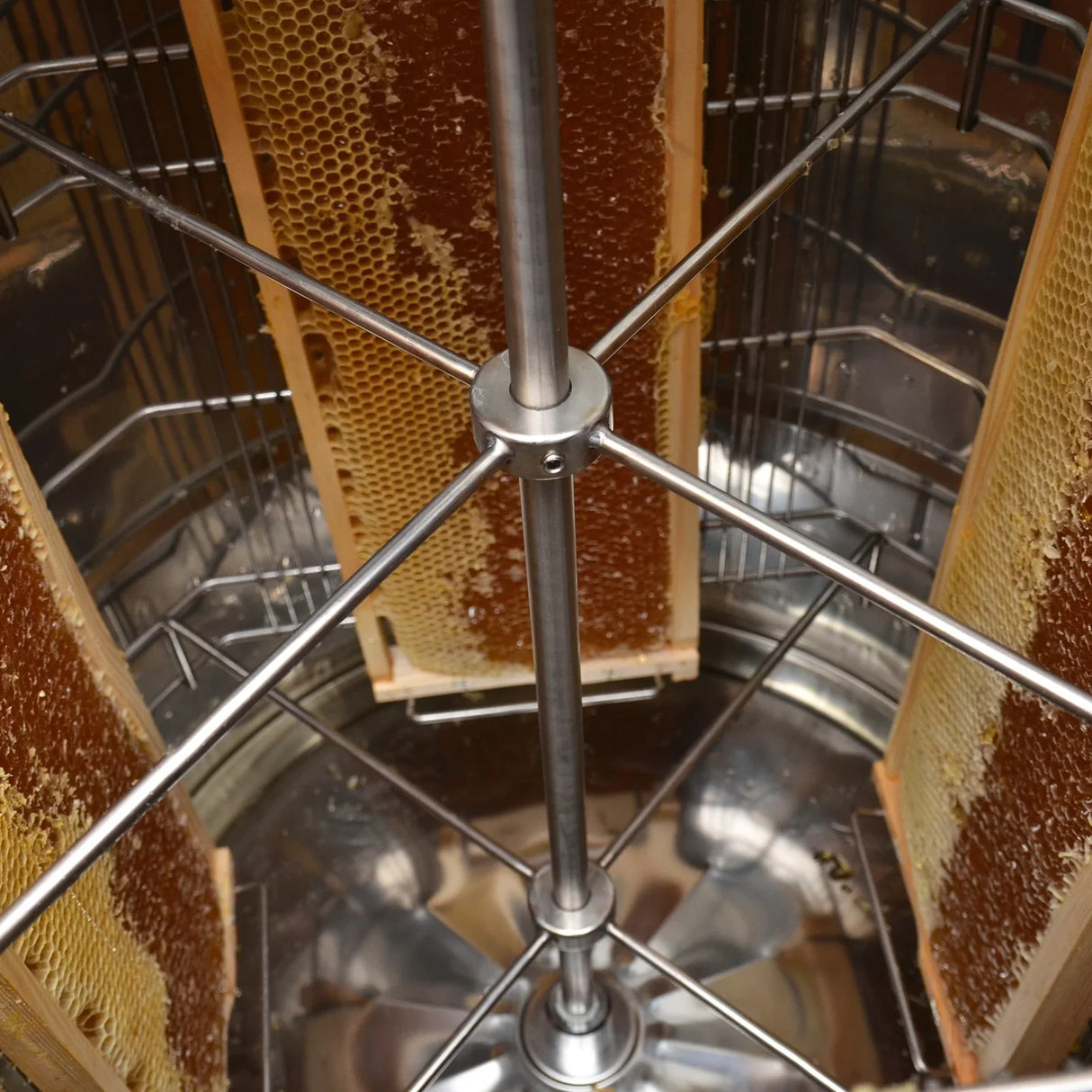 Manual honey extractor featuring stainless steel construction, with honeycomb frames positioned inside for efficient honey extraction