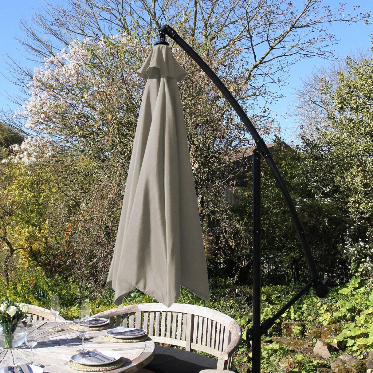 Beige cantilever parasol with a sleek black frame, elegantly shading a garden dining area surrounded by blooming trees