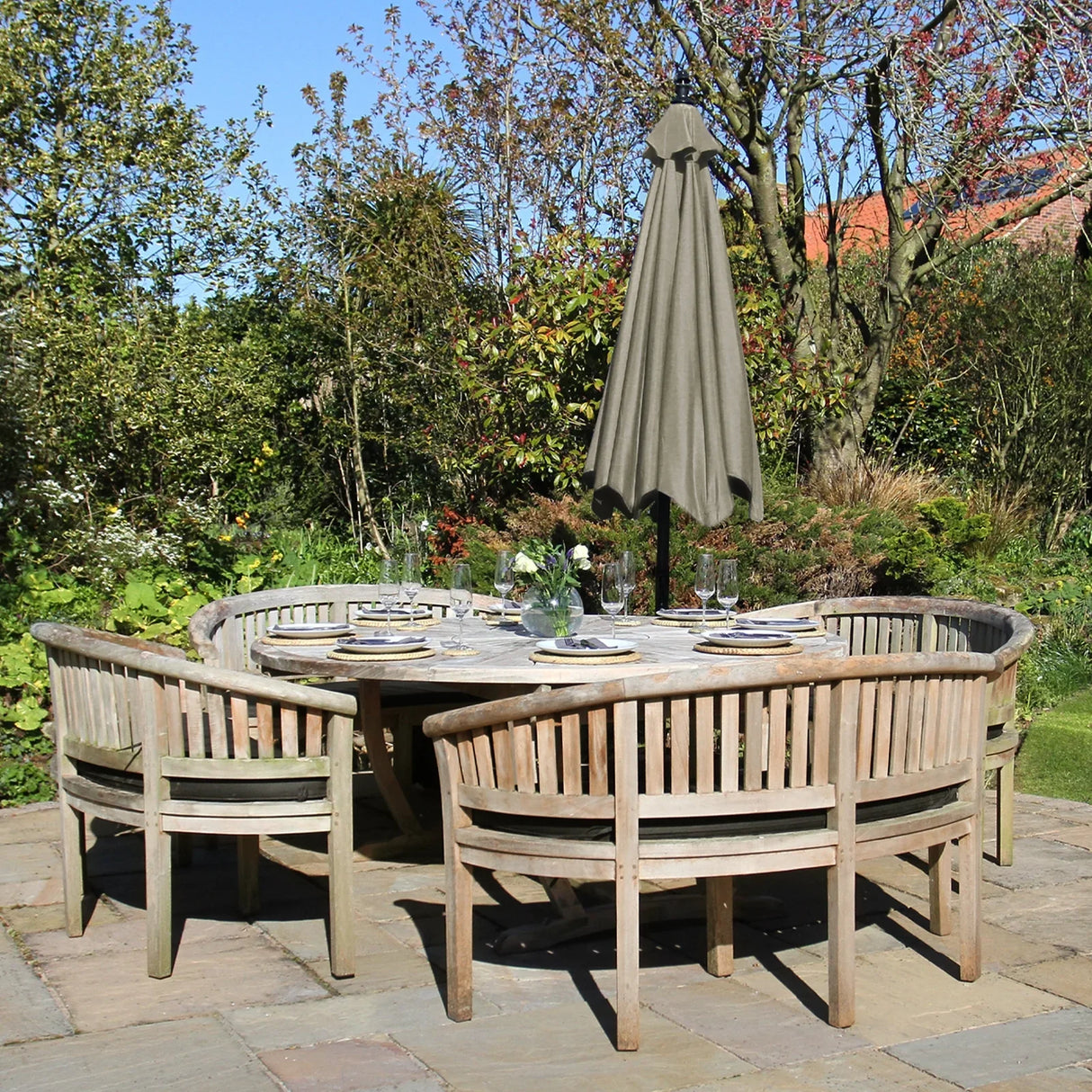 Beige cantilever parasol stands tall over a round wooden dining table surrounded by curved wooden chairs in a lush garden setting