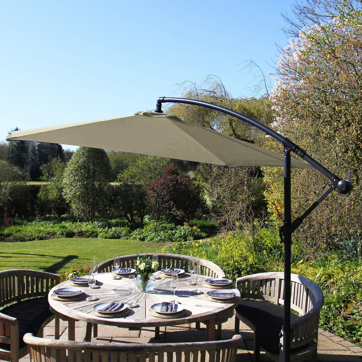 Beige cantilever parasol with a sturdy black frame, providing shade over a round wooden dining table set in a lush garden