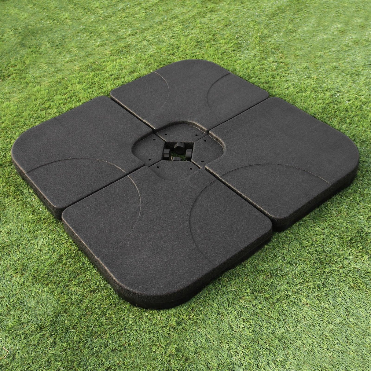 Black square base for a beige cantilever parasol, featuring a textured surface and four interlocking sections, set on green grass