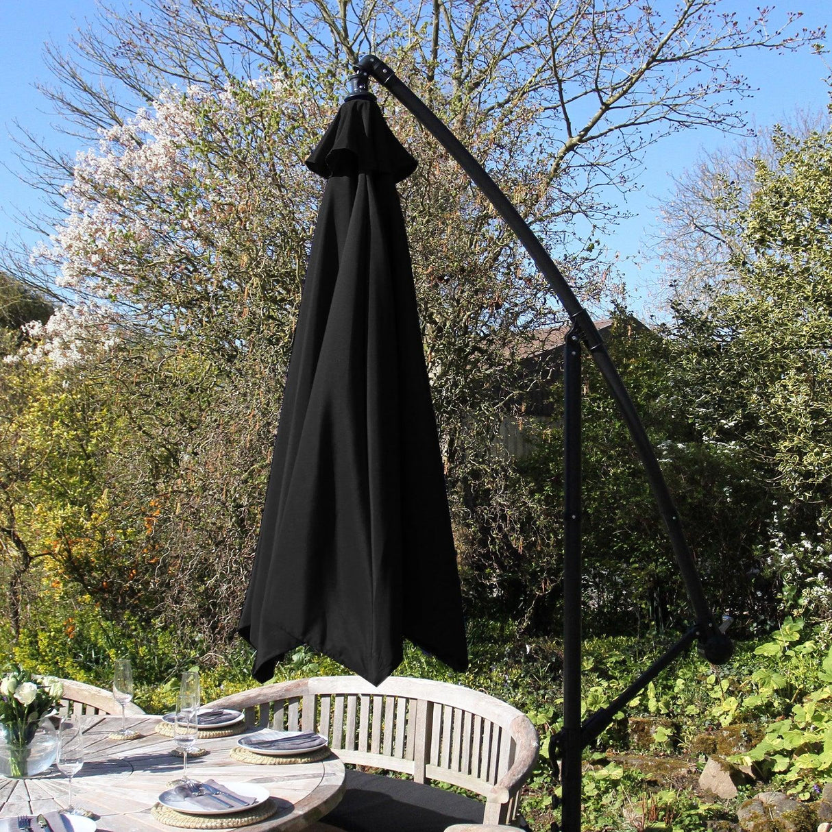 Black cantilever parasol with a sleek design, featuring a sturdy arm and a large, elegant canopy, set against a vibrant garden backdrop