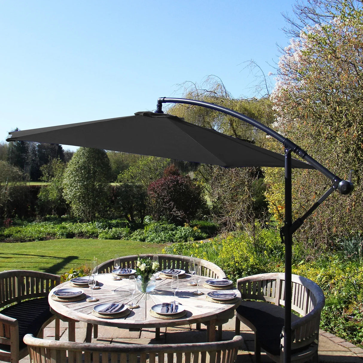 Black cantilever parasol with a sleek, modern design, providing shade over a round wooden dining table set in a lush garden