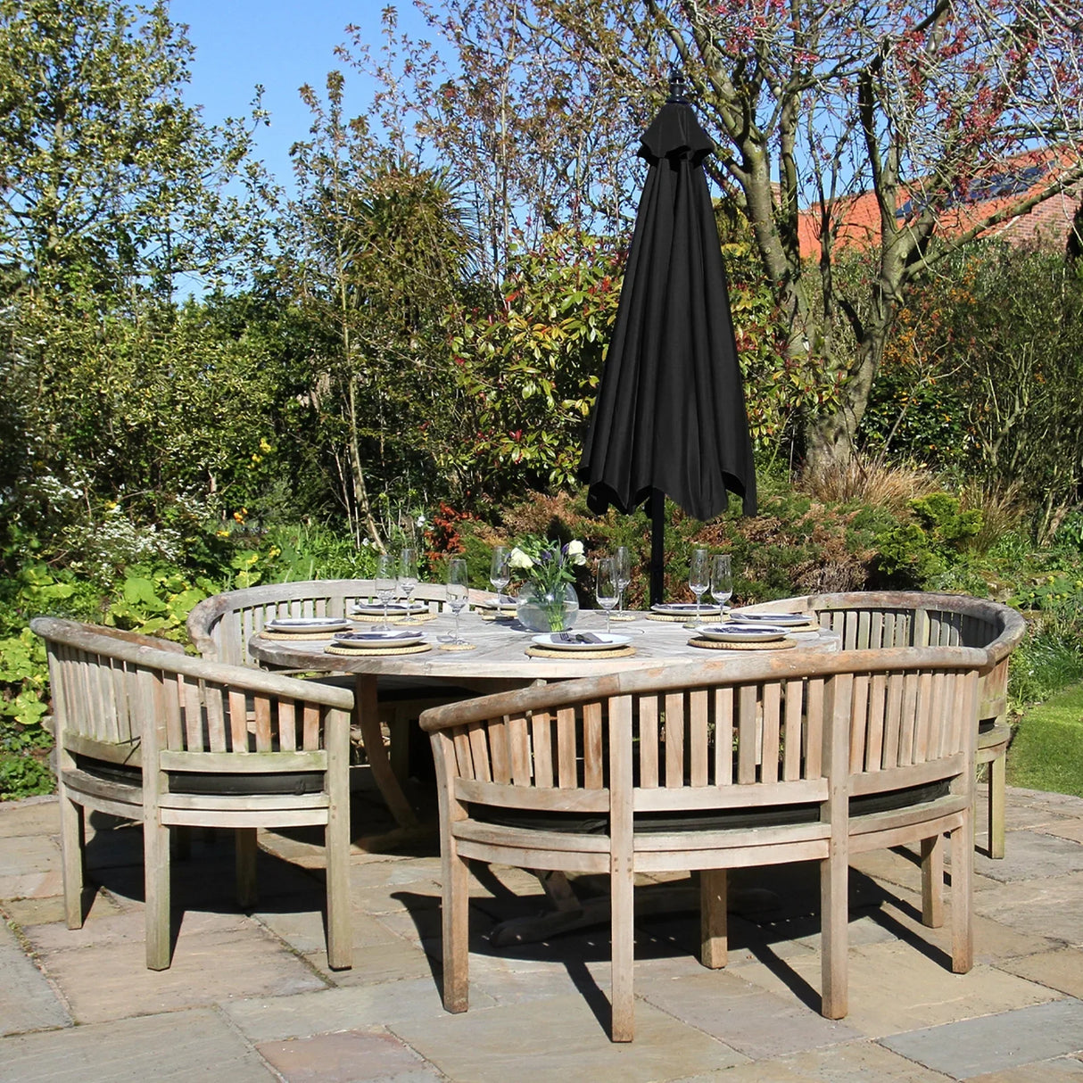 Black cantilever parasol stands tall above a rustic wooden dining set in a lush garden, providing shade and elegance to outdoor gatherings
