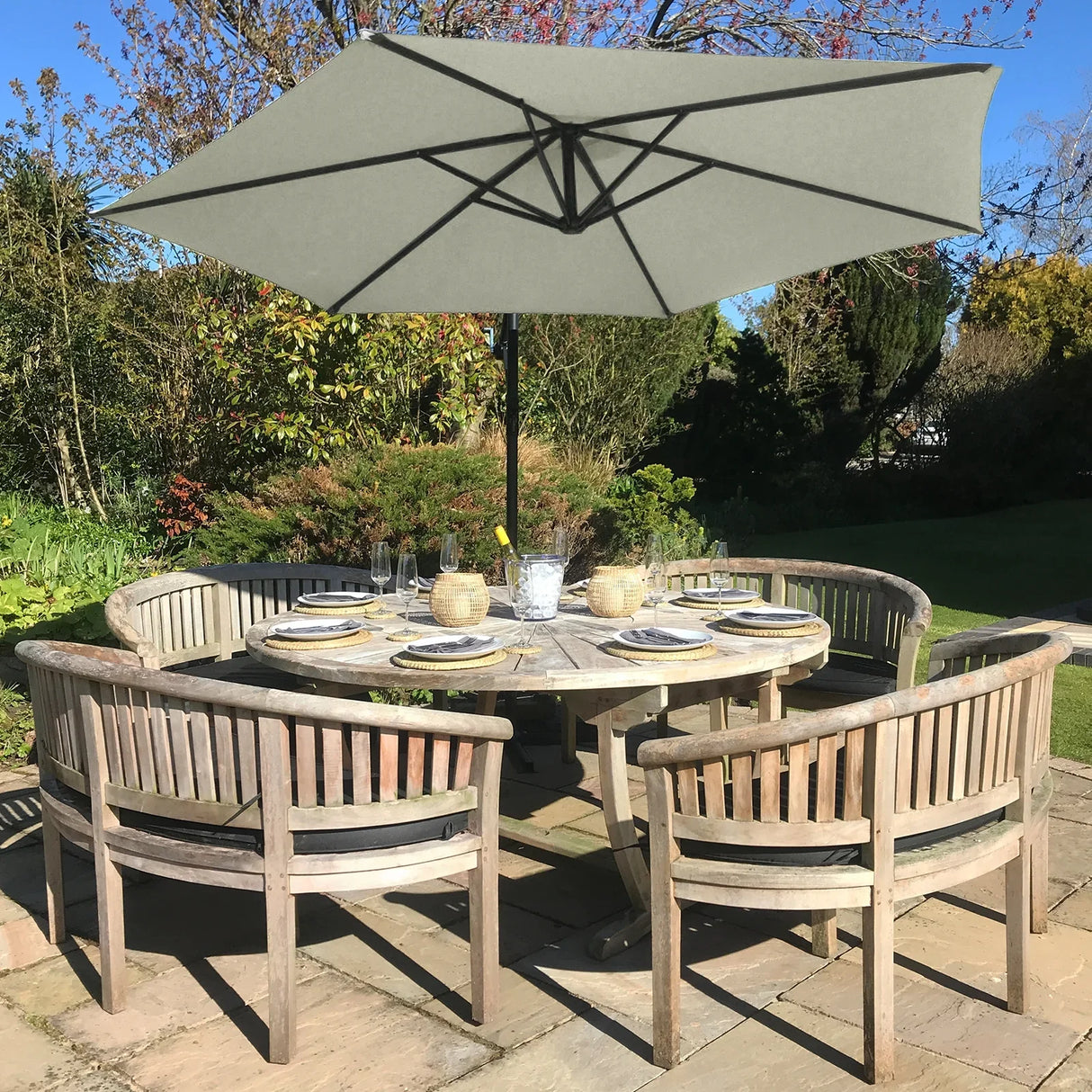 Cream cantilever parasol with a large gray canopy, providing shade over a rustic wooden dining table surrounded by curved chairs in a garden setting