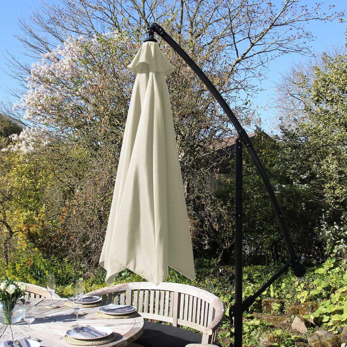 Cream cantilever parasol with a sleek black frame, elegantly draped fabric, providing shade over a stylish outdoor dining setup
