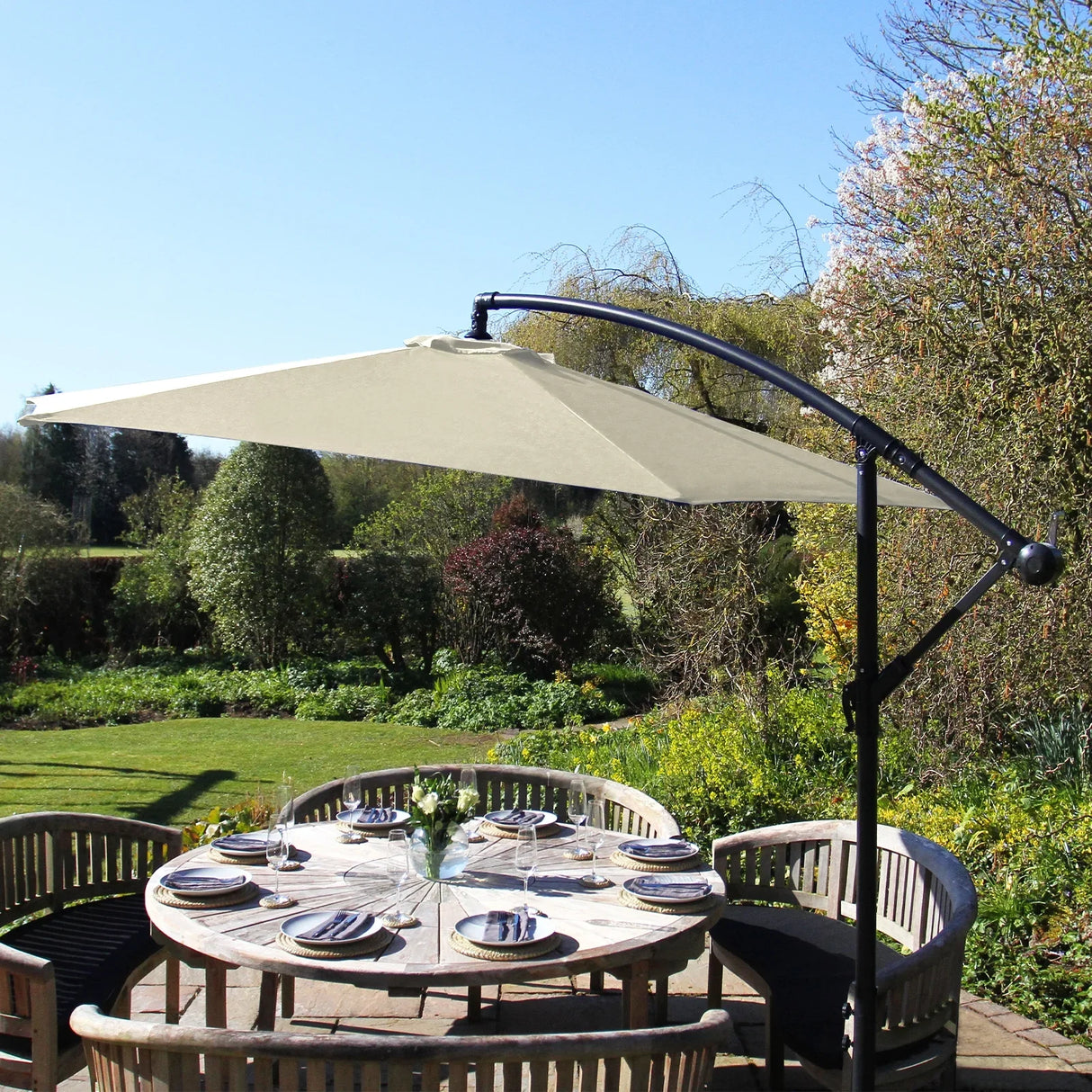 Cream cantilever parasol with a sleek black frame, providing shade over a round wooden dining table set in a lush garden