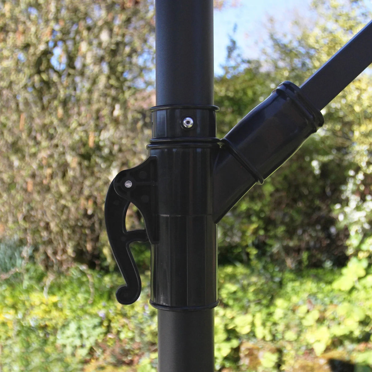 Close-up of the cream cantilever parasol's adjustable mechanism, showcasing a sleek black handle and sturdy pole against a garden backdrop
