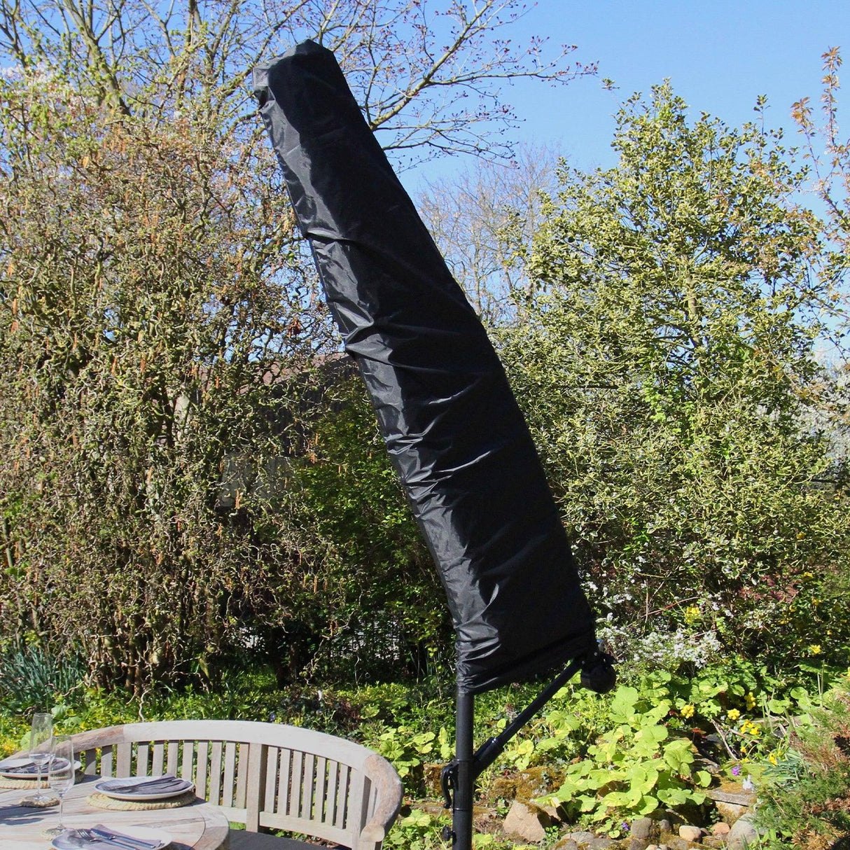 Cream cantilever parasol with a sleek black cover, standing tall against a garden backdrop, ideal for outdoor shading and style