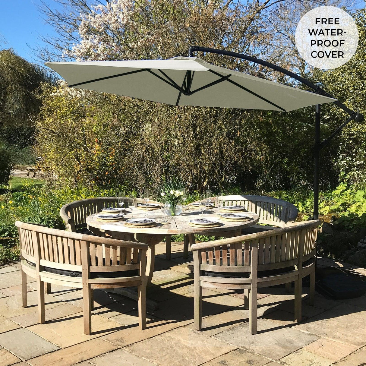 A cream cantilever parasol with a light canopy and black frame provides shade over a wooden dining table adorned with plates and flowers in a garden