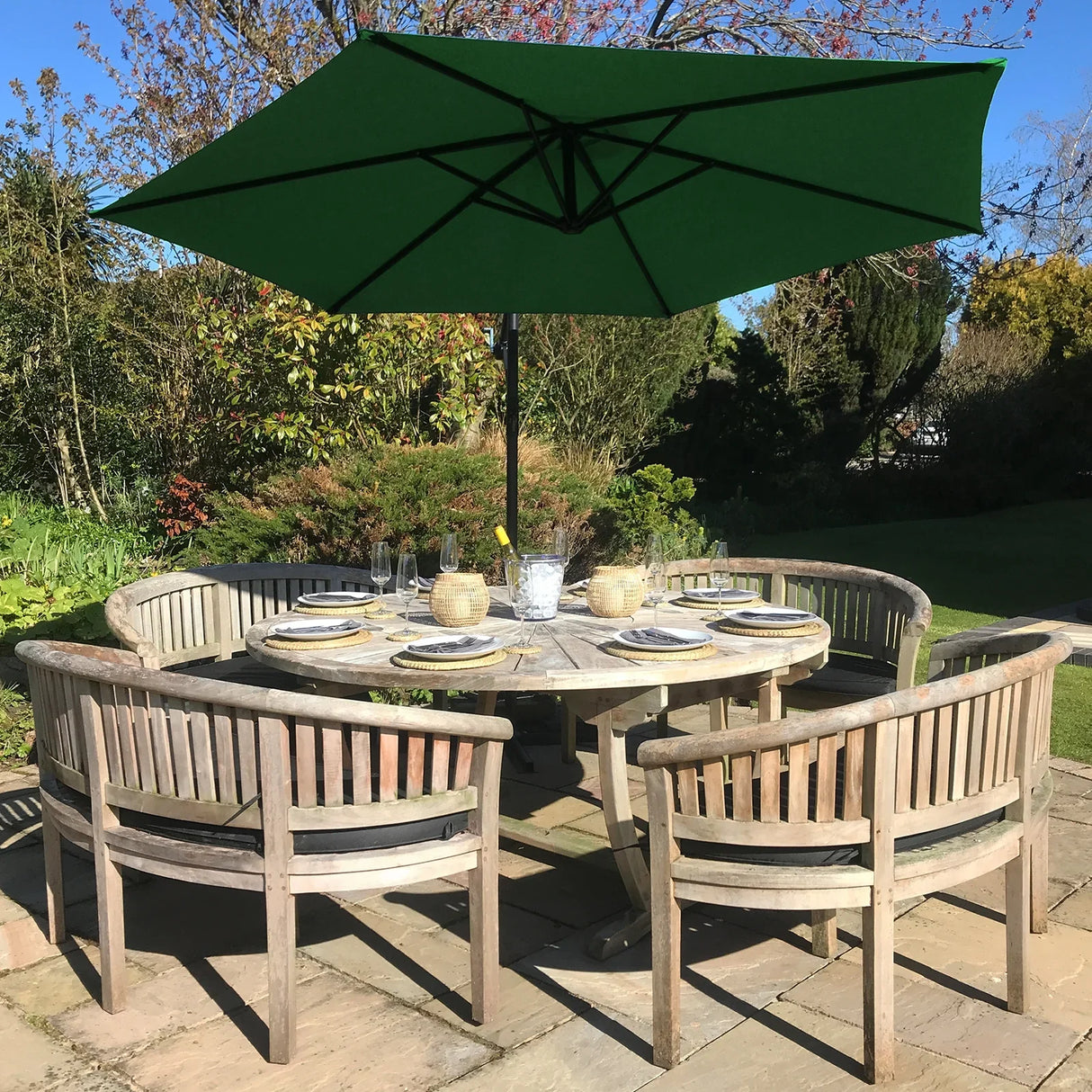 Green cantilever parasol with a wide canopy, providing shade over a round wooden dining table set with plates and glasses in a garden setting