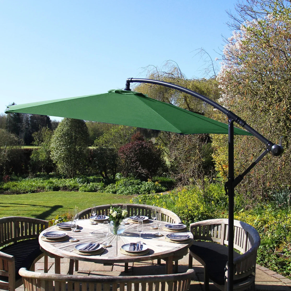 Green cantilever parasol with a wide canopy, supported by a sleek black frame, shading a round wooden dining table in a sunny garden setting