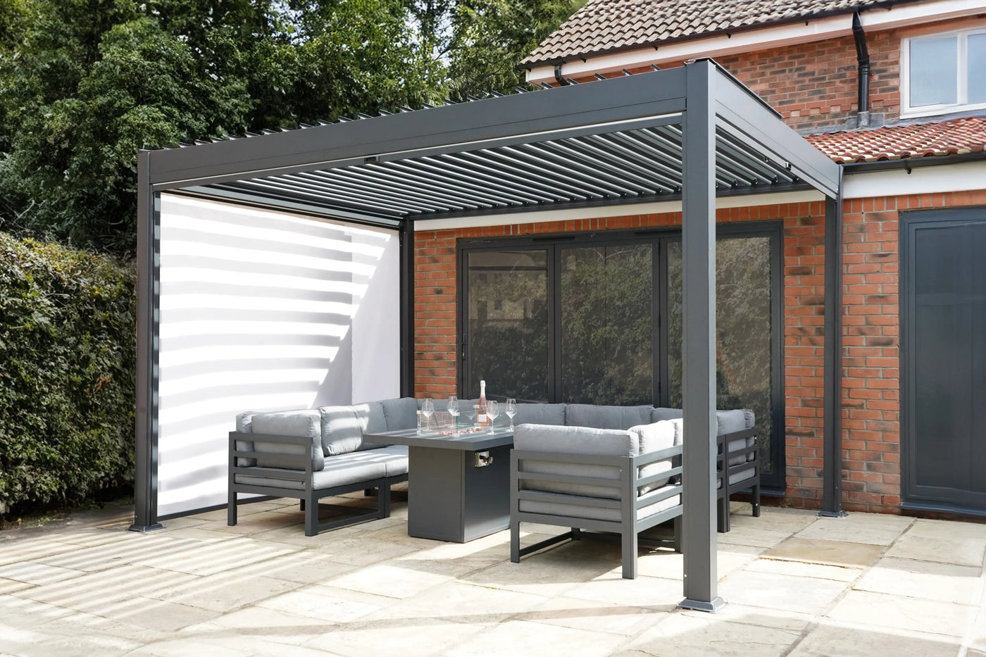 Modern outdoor patio with a sleek gray pergola, comfortable gray seating, and a glass-top table, surrounded by greenery