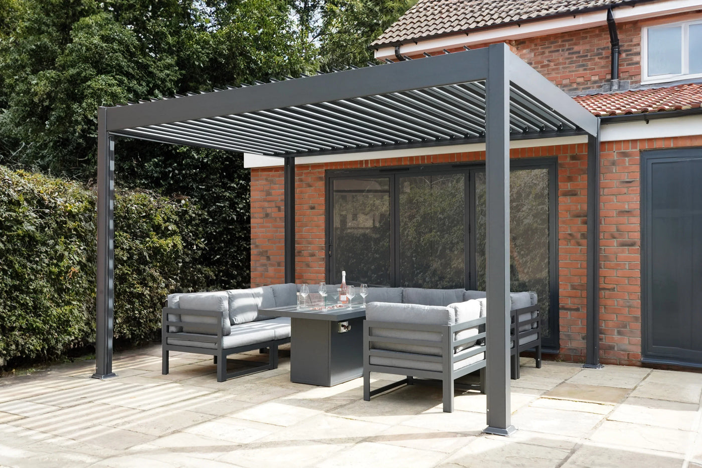 Modern outdoor patio with a sleek gray pergola, comfortable gray seating, and a glass-top table, surrounded by greenery