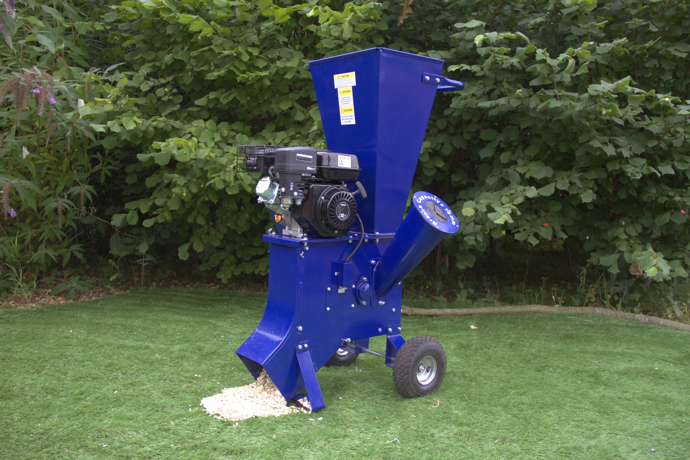 Blue wood chipper on wheels with a powerful engine, designed for shredding branches and yard debris, set against lush greenery
